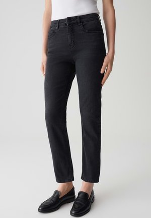 Zwarte denim jeans met een slim fit, vijf zakken, een sluiting met knoop aan de voorkant en subtiele wassingdetails. Gecombineerd met zwarte instappers.