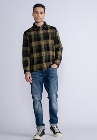 Schwarzes und grünes karierter Flanellhemd mit Knöpfen, kombiniert mit ausgewaschenen blauen Jeans und schwarzen Sneakern mit weißen Sohlen.