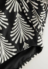 Čierny textil so vzorom bielych listov. Textúra je hladká s úpravným detailom pozdĺž okrajov.