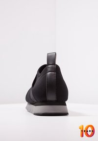 Svart aktivitetsko med en slät yta, elastisk tyg och en solid häl. Har en grå sula och en liten bakre dragflik.