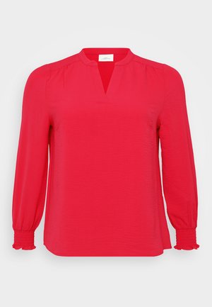 Blouse en crêpe rouge avec un décolleté en V, manches bouffantes longues avec des poignets élastiques, et une coupe légèrement décontractée. Texture lisse avec un éclat subtil.
