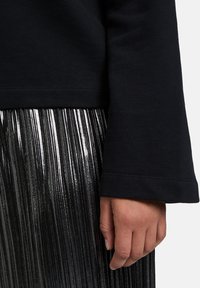 Felpa nera a maniche lunghe con polsini ampi, abbinata a una gonna plissettata di colore argento metallico. La texture sembra liscia e lucida.