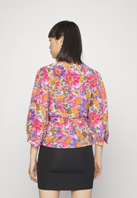 Blusa floral com padrões coloridos de flores rosa, laranja e roxas. Possui mangas longas e cintura ajustada. Saia preta por baixo.