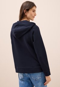 Hoodie bleu marine en coton, avec une capuche à cordon de serrage et une coupe décontractée. Texture lisse avec des poignets et un ourlet côtelés.