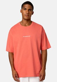 Coral crew neck t-shirt in soft cotton fabric with short sleeves, featuring white text "ON VACATION CLUB" across the chest.