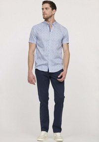 Chemise à manches courtes, bleu clair, avec un motif floral, assortie à un pantalon bleu foncé et des baskets blanches. Fermeture à bouton simple, coupe décontractée.