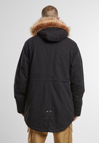 Fekete parka dzseki szőrmebéléses kapucnival, hosszított szabással, felhajtható ujjal és patentos záródással a hát alján. Tartós szövet textúra.