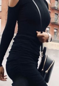 Black cold-shoulder dress with ruched detailing, paired with a small black crossbody bag, silver watch on wrist. Urban backdrop visible.