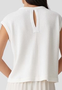 Witte gebreide top met korte mouwen, met een sleutelgat aan de achterkant. Textuurstof en een relaxte pasvorm met een rechte zoom.