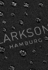 Tessuto nero testurizzato con gocce d'acqua sulla superficie. Il testo "CLARKSON HAMBURG" è parzialmente visibile, stampato in modo sottile.