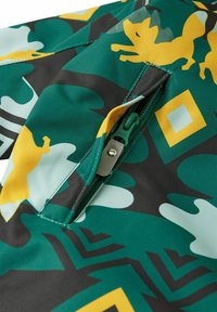 Tissu vert avec un motif camouflage, comportant des renards jaunes et des formes géométriques ; comprend une fermeture éclair verte et des ferrures en métal.