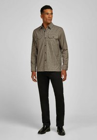 Gecarreerde button-up shirt in bruin en beige, met twee borstzakken, gedragen met zwarte broek en zwarte enkellaarzen. Vlakke textuur.