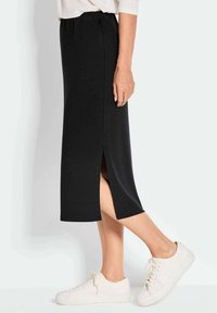 Jupe noire mi-longue avec une fente sur le côté, fabriquée en tissu doux. Associée à des baskets blanches pour un look décontracté. Taille élastique pour le confort.