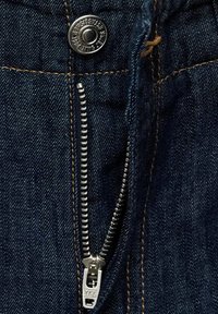 Donkerblauwe denimstof met een zilveren metalen rits en knoop. Close-up toont stikseldetails en het ritsmerk "YKK."