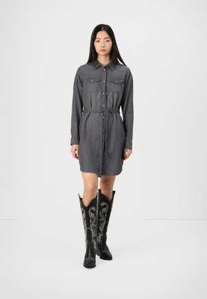 Grå denimskjorte kjole med beltestykke i midjen, lange ermer og to brystlommer, kombinert med høye svarte broderte cowboy støvler.