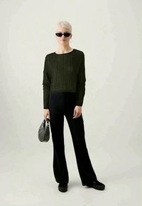 Melni plati bikses apvienoti ar olīvu zaļas ribotas garas piedurknes blūzes. Pievienoti aksesuāri: neliela pelēka rokassoma un melni saulesbrilles.