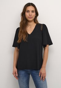 Top nero a scollo a V con maniche corte e larghe e accenti testurizzati sulle spalle. Tessuto morbido con una vestibilità rilassata, abbinato a jeans blu.