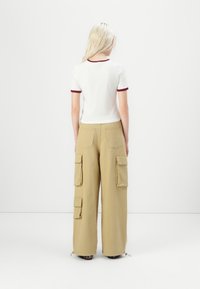 White short-sleeve top with maroon trim paired with loose beige cargo pants featuring multiple pockets and cuffs at the hem.