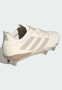 Vit fotbollssko med beige accenter, slät ovandel och tre randig design. Inkluderar metalliska dobbar för grepp på gräsytor.