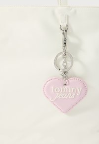 Valge käekott roosa südamekujulise nahast võtmehoidjaga, millel on tikitud tekst "tommy jeans" ja hõbedased riistvarakaunistused.