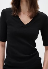 Svart ribbad topp med V-ringning, kortärmar och strukturerad väv. Designen är figurnära med subtil strech och en ren finish.