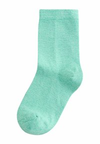 Vienas žalias čiurnos kojinėlis iš minkštos megztos medžiagos, paplotas, matomas padas ir pirštai, baltoje fone.