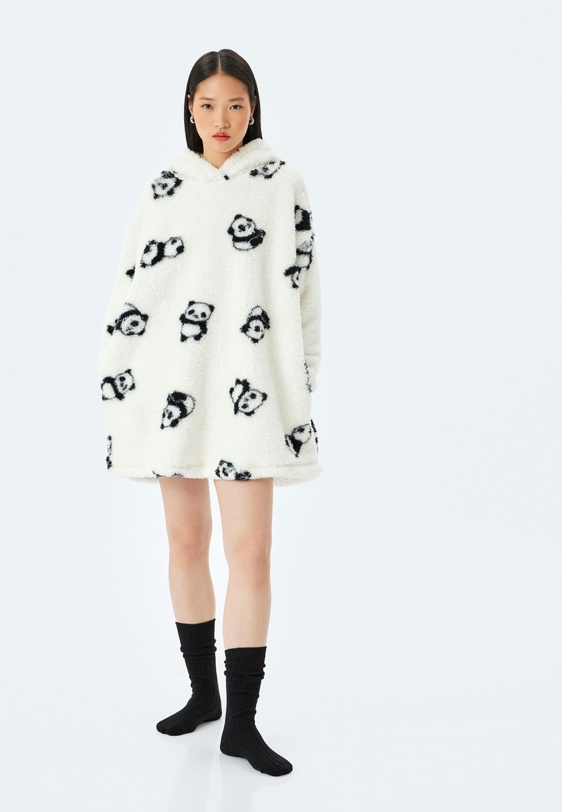 Sudadera blanca de felpa con estampado de pandas negros, diseño oversized, textura suave y bolsillo tipo canguro, combinada con calcetas negras de canalé.