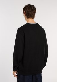 Schwarzer Pullover mit Rundhalsausschnitt, gerippten Ärmelbündchen und -saum. Gerippte Textur mit lockerer Passform, ausgestattet mit einem weißen Akzent am Kragen.