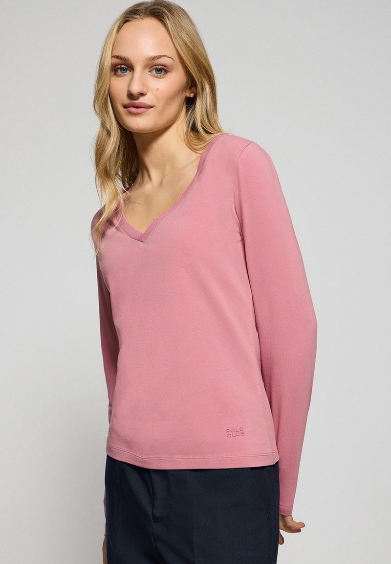 Långärmad rosa t-shirt med v-ringning, tillverkad av mjukt material, med en avslappnad passform och diskret logotypdetalj vid fållen.