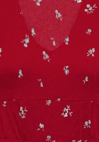 Tissu rouge avec petit motif floral blanc et encolure en V, montrant une texture détaillée et une couture à la taille.