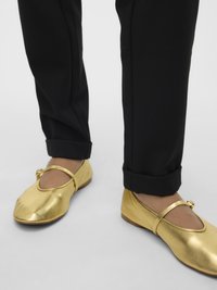 Metāla zelta baleta dzīvokļi ar noapaļotu purngalu un vienu siksniņu pāri pēdai. Kombinēti ar melnām, atlocītām biksēm. Gluda tekstūra.