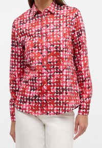 Long-sleeve shirt featuring a vibrant pattern of red, pink, and black circles on a white background. Button-down collar and cuffed sleeves.