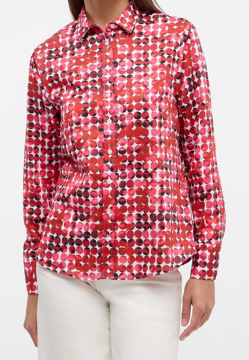 Long-sleeve shirt featuring a vibrant pattern of red, pink, and black circles on a white background. Button-down collar and cuffed sleeves.