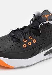 Basket de basketball noire et orange avec lacets noirs, œillets orange, cuir perforé, semelle intermédiaire blanche et logo Jumpman sur la languette.