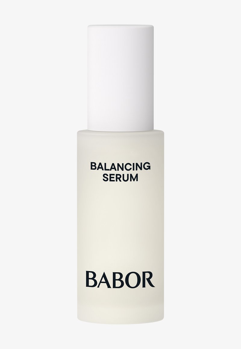 Een serumfles met een doorschijnende, frosted glazen basis en een witte cilinderkap; voorzien van een zwart tekstlabel voor productidentificatie.