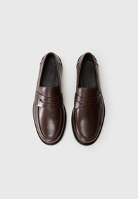 Braune Lederloafers mit glatter Oberfläche, einem dekorativen Riemen quer über der Oberseite und einem runden Zehenbereich mit schwarzen Gummisohlen.