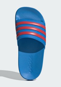 Niebieska klapka na ślizg z trzema czerwonymi paskami na górze, teksturowanym materiałem i wytłoczonym logo "adidas" na wkładce.