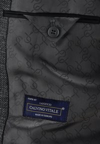Graues Stoffinnere eines maßgeschneiderten Kleidungsstücks mit Knopfverschluss, glatter Textur und einem blauen Etikett mit der Aufschrift "Calvino Vitale, Made in Europe."