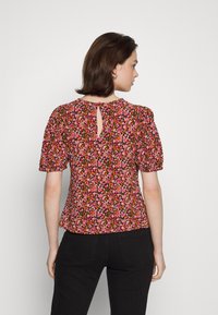 Blusa floral em rosa, laranja e preto com mangas curtas bufantes e uma abertura em forma de chave nas costas. Tecido suave com um acabamento texturizado.