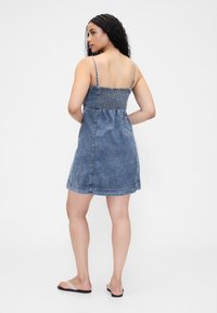 Džínové šaty s přiléhavým živůtkem a rozšířenou sukní. Mají tenká ramínka a na zádech pružné našití ve středně modrém odstínu.