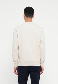 Felpa beige chiaro con polsini e orlo a coste. Realizzata in tessuto morbido e testurizzato. Design a girocollo, con un retro semplice e lineare.