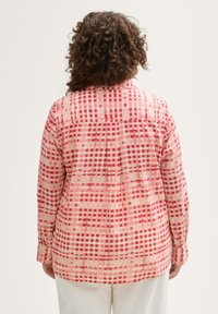 Chemise à manches longues avec un motif à carreaux rose et rouge. Fabriquée dans un tissu léger avec une coupe ample et des poignets boutonnés. Détail de l'empiècement au dos inclus.