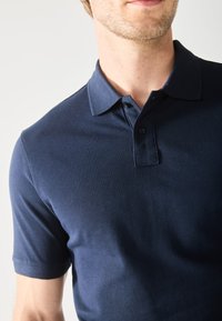 Polo bleu marine avec un col, des manches courtes et une patte de boutonnage à trois boutons, fabriqué en tissu texturé.