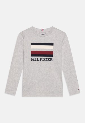 Jasnoszara koszula z długim rękawem z dwoma prostokątnymi blokami kolorystycznymi w granacie, kremowym i czerwonym nad słowem "HILFIGER" granatowymi literami.