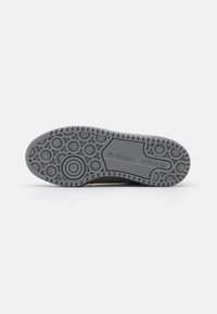 Gray sneaker outsole with circular traction pattern, featuring branded accents and ridged texture. Durable rubber material.