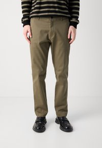 Chino de culoare verde oliv, cu o croială slim, realizat din țesătură de bumbac. Are buzunare laterale și închidere cu nasture, fiind asortat cu mocasini negri.