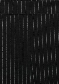 Svart tyg med vertikala vita ränder, med en strukturerad väv. Designen inkluderar en midjeband och en liten slits i botten.