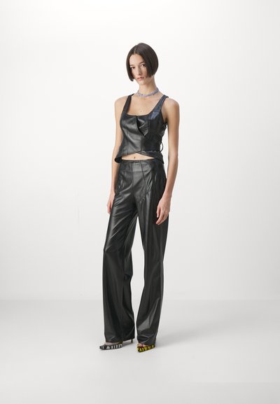 Fekete bőr crop top és széles lábú nadrág, amelyek testre simuló kialakítással és sima textúrával rendelkeznek. A modellen színes, mintás magassarkú cipők találhatók.