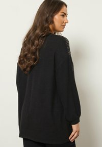 Czarny, oversize sweter z długimi rękawami, z fakturowanym splotem na ramionach i luźnym krojem. Miękka tkanina i okrągły dół. Widok z tyłu.