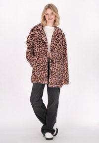 Abrigo de piel sintética de leopardo rosa con cuello oversize, botones frontales y bolsillos laterales, combinado con jeans negros y zapatillas blancas.